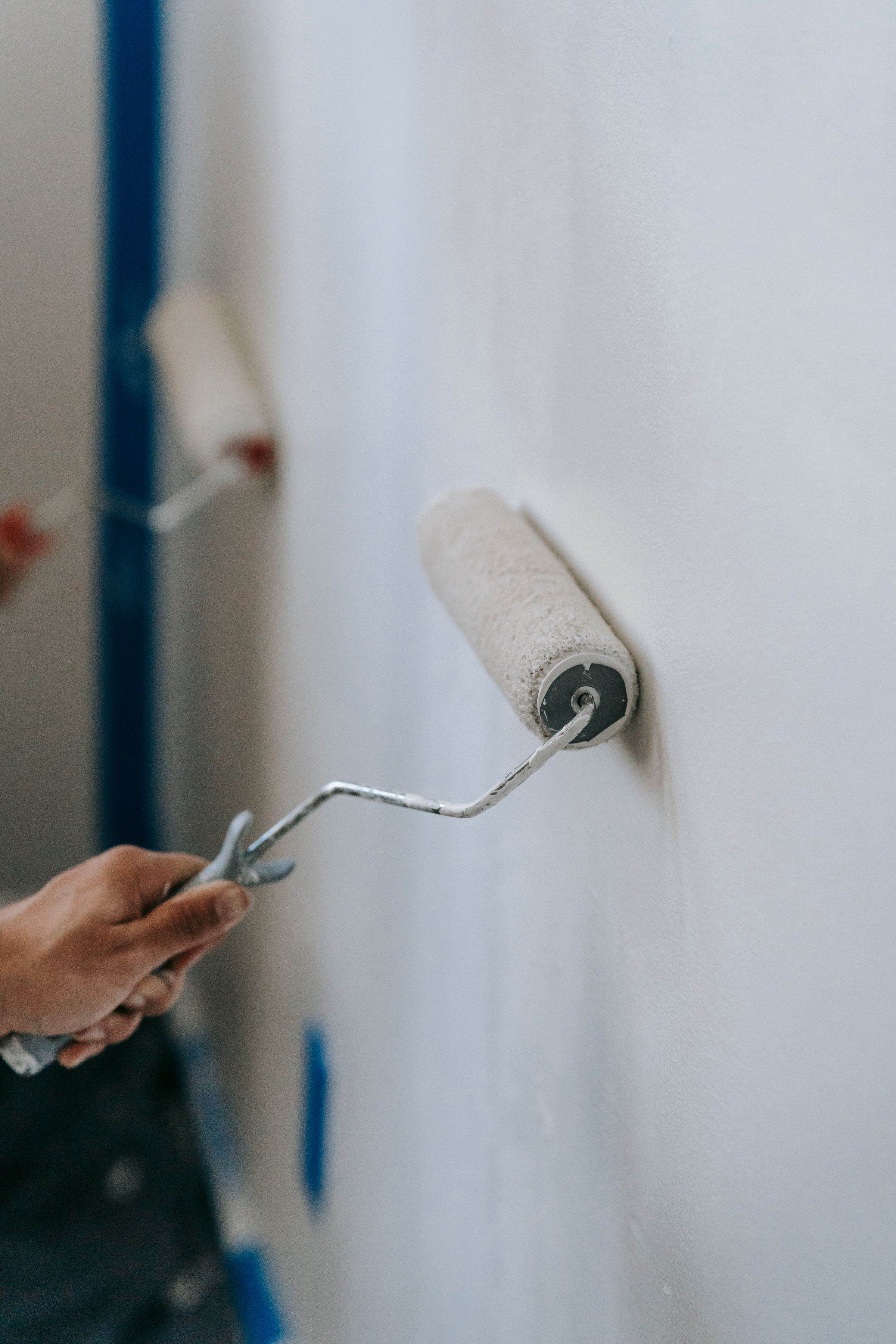 Paint roller applying white paint next to a taped edge